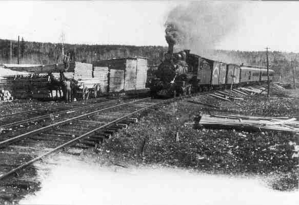 This undated photo shows a mixed train of the Canadian Northern headed by a 2-6-0 Mogul (either 107 or 108) moving past piles wood and lumber stacked alongside the tracks. The photo was most likely taken in the 1910's somewhere near Nolalu.